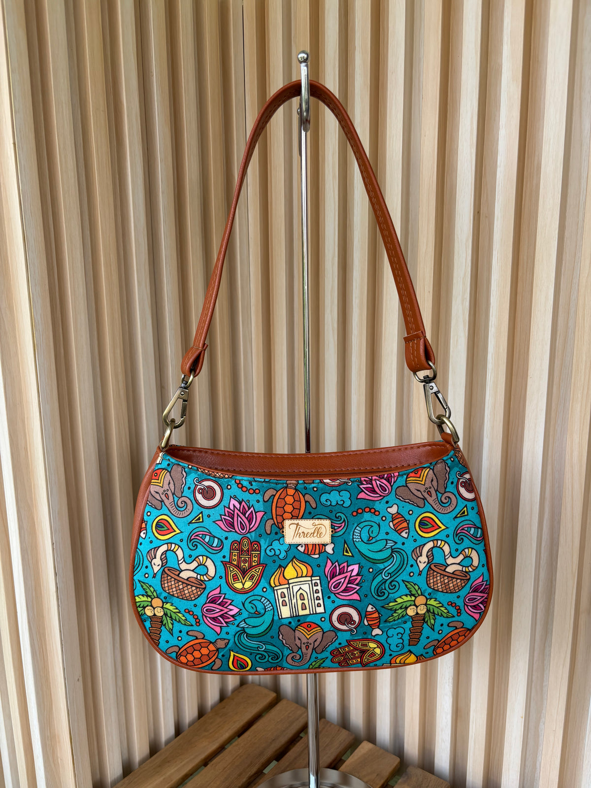 India Print Baguette Bag in tan, hanging by its tan strap: elephants, lotuses and palaces on turquoise