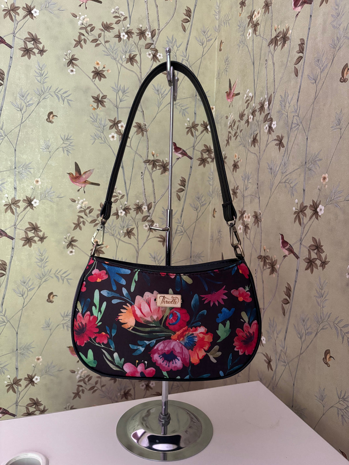 Night Garden Baguette Bag hanging by its black strap: watercolour flowers on black