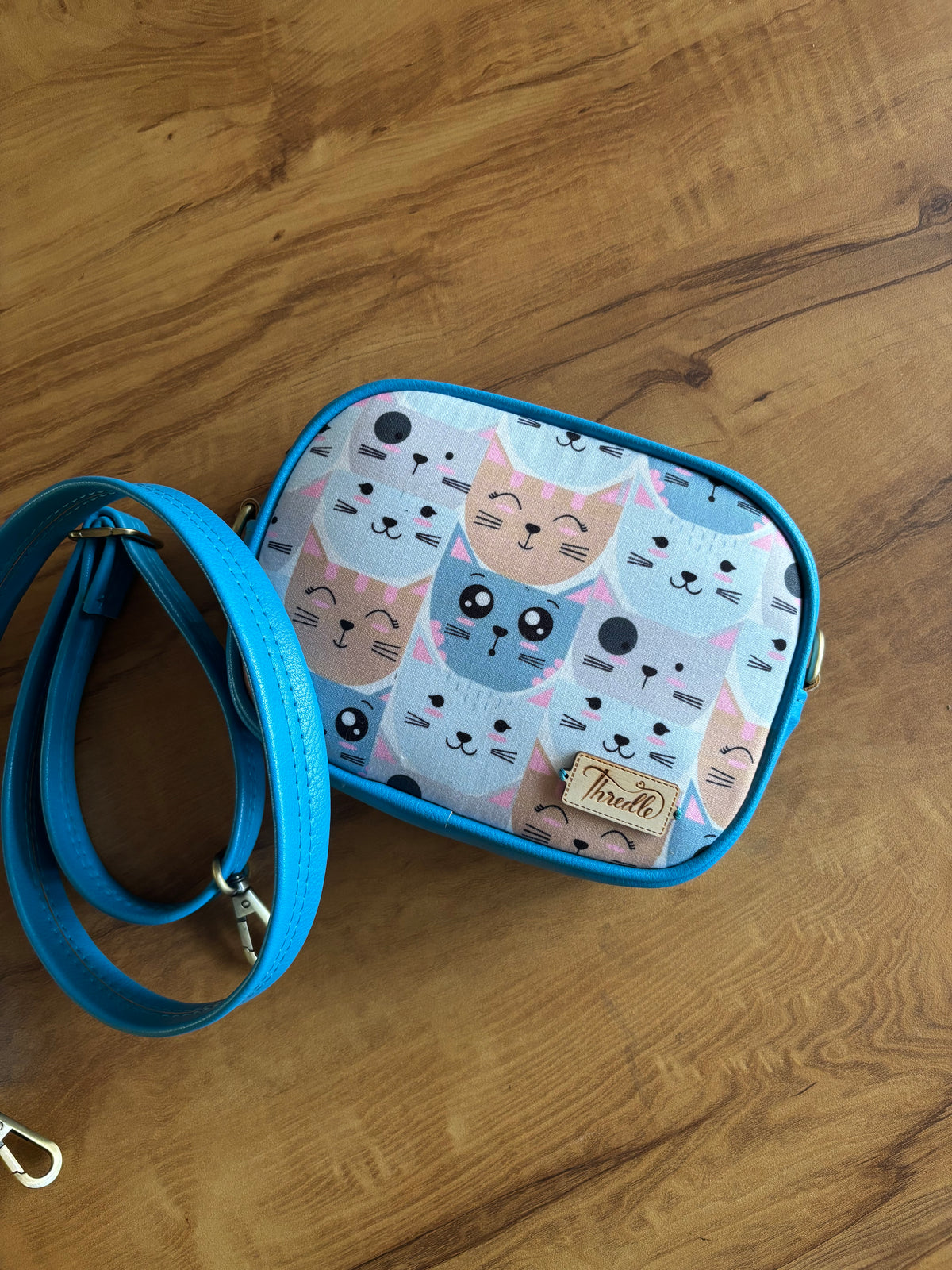 Pastel Cat Print Sling in blue, lying flat with its matching blue strap