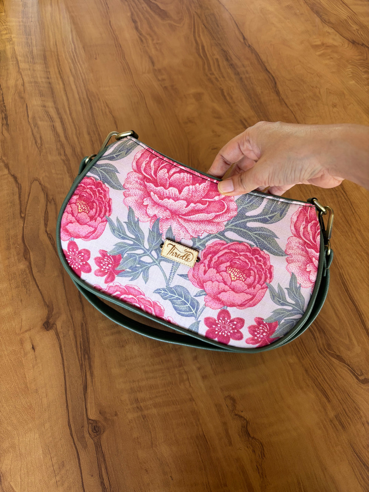 Peony Garden Baguette Bag held in hand: pink peonies on cream, framed in sage green