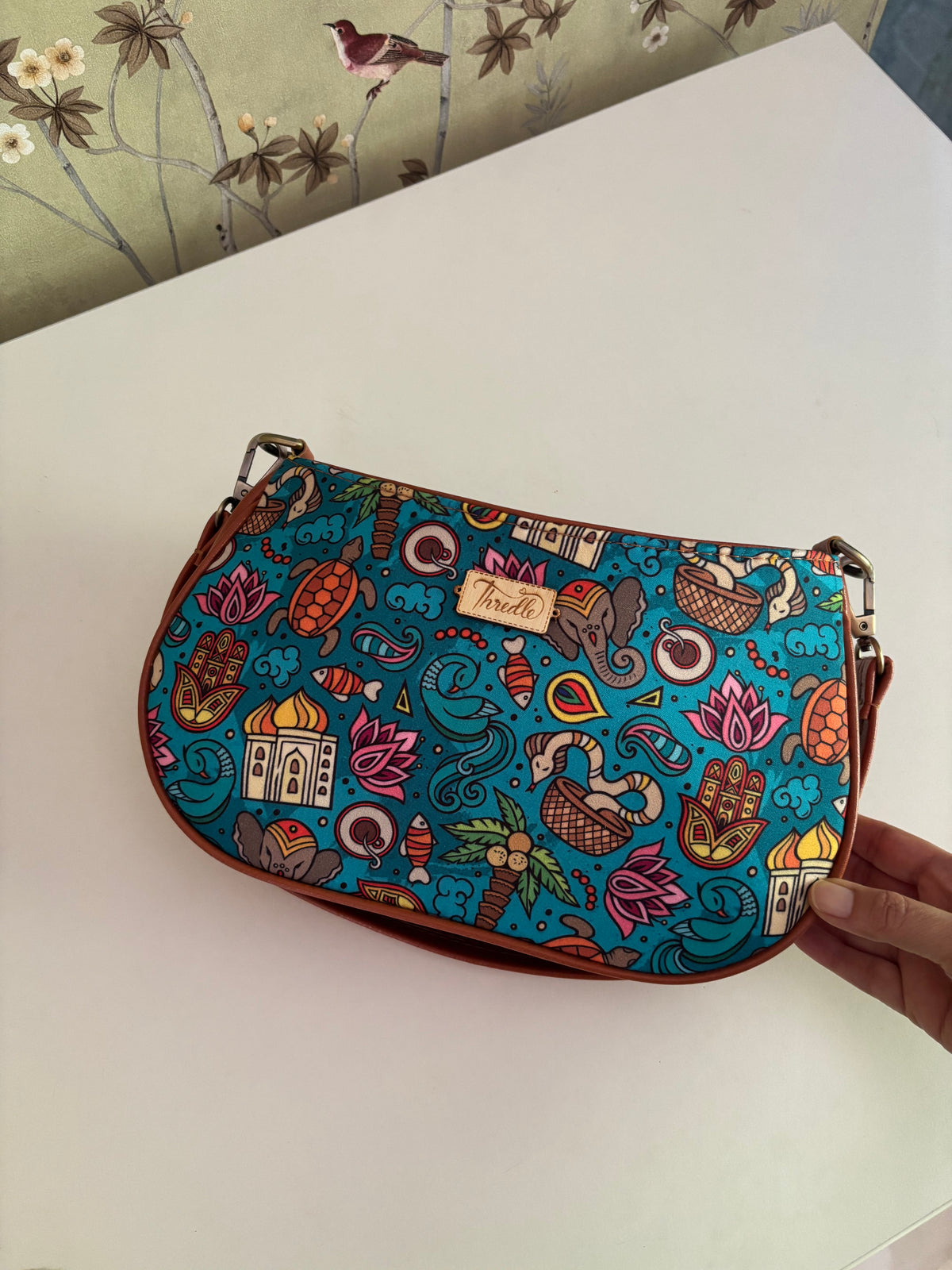 India Print Baguette Bag held in hand, front view of the turquoise India print